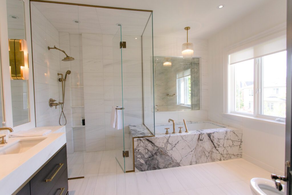 A marble bathtub and glass shower doors in a bright and airy white bathroom.