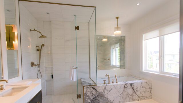 A marble bathtub and glass shower doors in a bright and airy white bathroom.